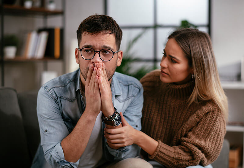A man and woman sit on a couch, hands to their faces, visibly experiencing paranoia in Dallas, TX