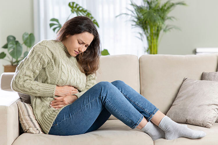 A woman sits on a couch holding her stomach due to anxiety causing nausea and vomiting in Dallas, TX