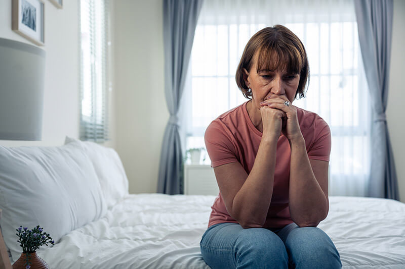 A woman sitting on her bed, visibly grieving and emotional