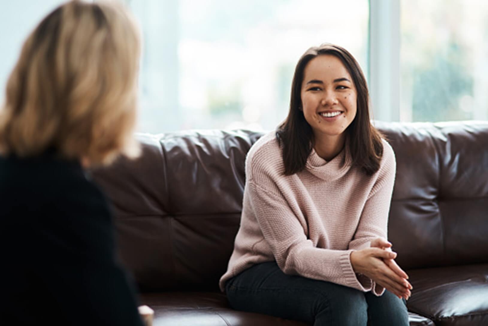 A smiling patient sits on a sofa talking with her psychiatrist about starting Spravato treatment