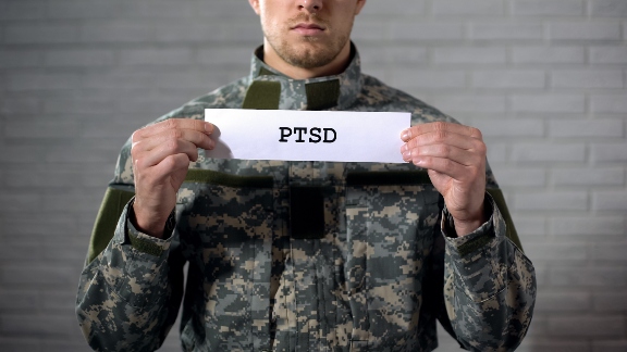 Person in military uniform holding a card labeled PTSD