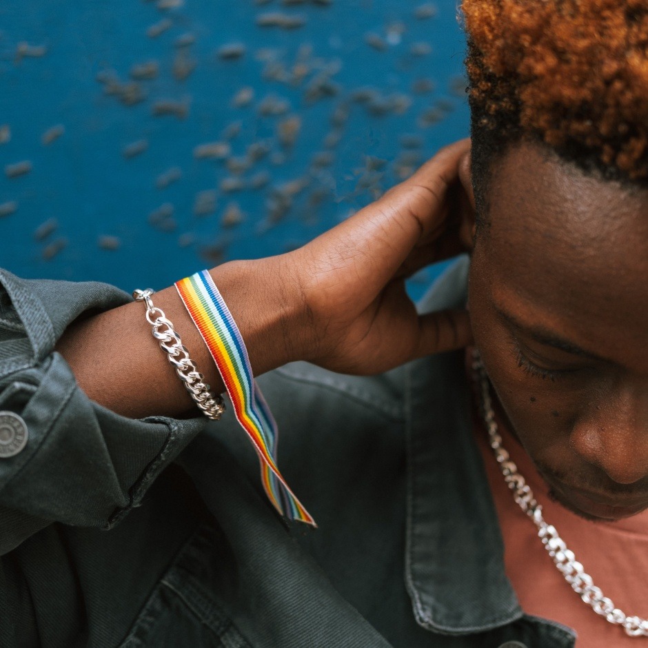 man with rainbow PRIDE bracelet looking down pensively
